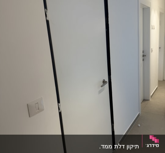 דלת ממ"ד לבנה מותקנת בבית עם משקוף כהה וידית נירוסטה